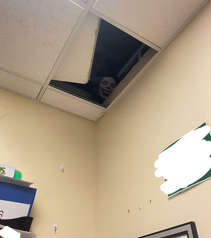 Figura con rostro aterrador asomándose por un techo falso en una oficina, ejemplo de humor ingenioso y sarcástico.