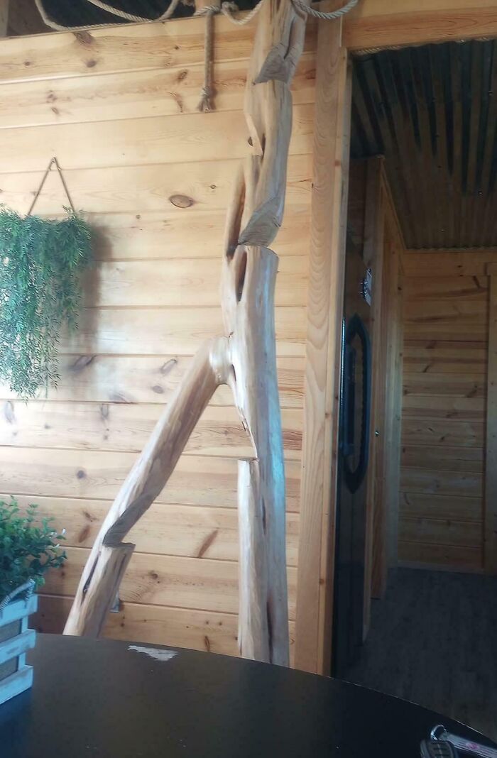Barandal de madera casero mal instalado en habitación de paredes y techo de madera rústica con plantas decorativas.