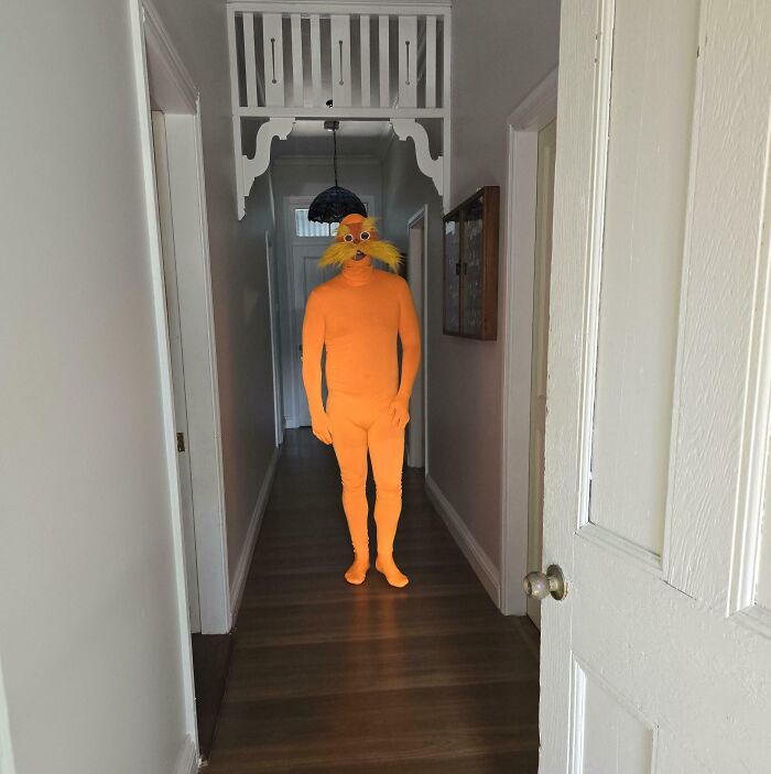 Persona disfrazada con traje casero naranja y bigote falso en un pasillo, ejemplo de proyectos caseros fallidos.