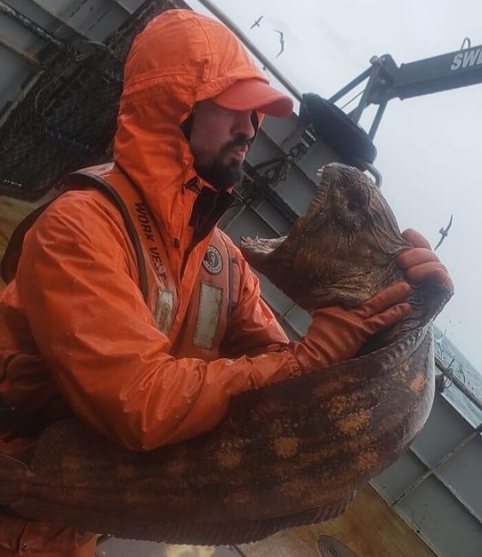 Hombre vestido de naranja sosteniendo un pez aterrador, foto aterradora que provoca heebie-jeebies en un barco.