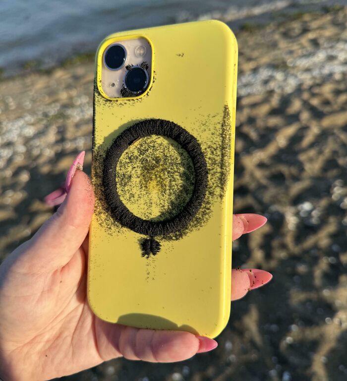 Mano sosteniendo un teléfono amarillo con un dibujo en arena magnética, inesperado hallazgo en la playa.