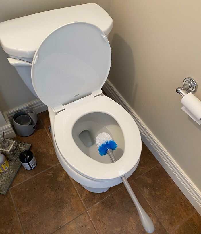 Inodoro blanco abierto con cepillo de limpieza dentro, mostrando uno de los life hacks geniales que la gente usa.