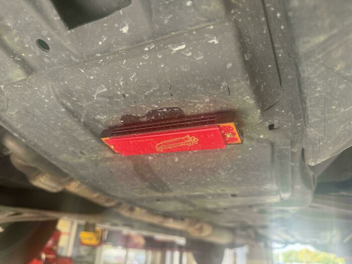 Dispositivo rojo pegado bajo un coche sucio, foto tomada por mecánicos de autos para mostrar evidencia visual.