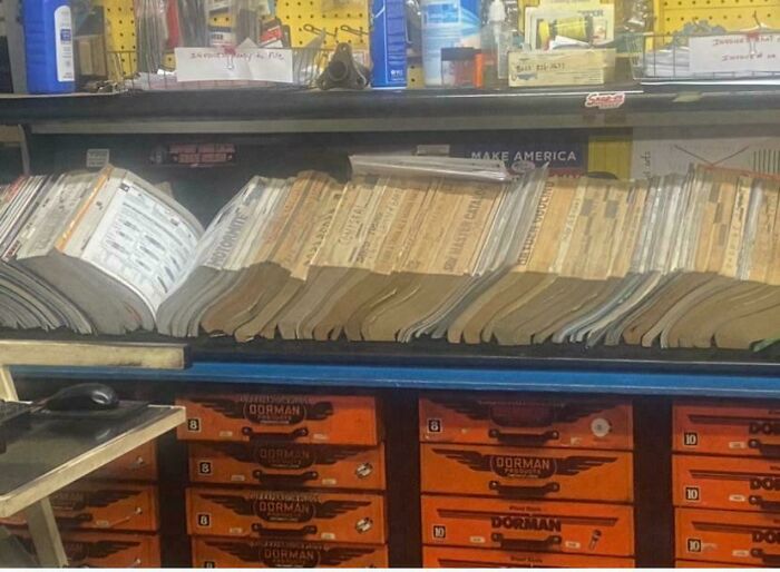 Manuales de reparación automotriz organizados en un taller, herramienta y productos para mecánica de autos al fondo.