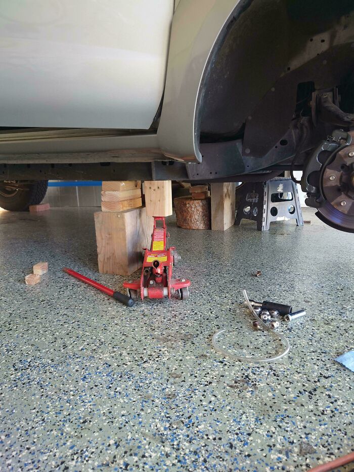 Gato hidráulico levantando coche sostenido con bloques de madera, vista del mecánico para pruebas y reparaciones.