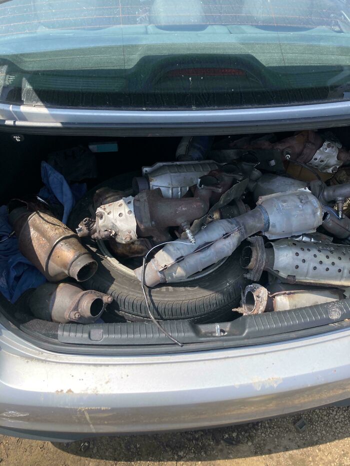 Maletero de coche lleno de catalizadores usados, mecánicos mostrando piezas para que otros les crean en el taller automotriz.