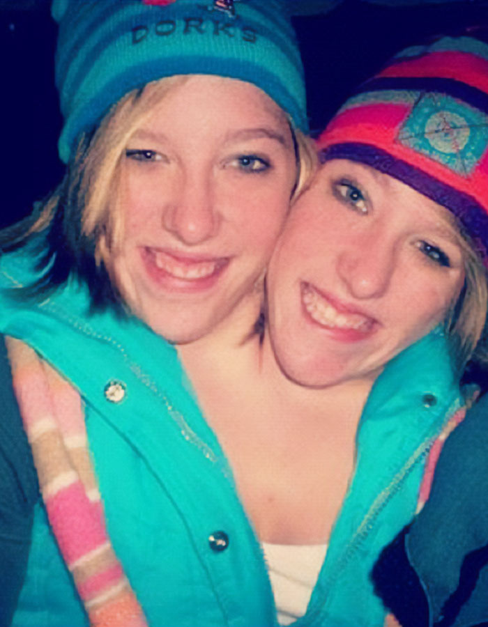 Siamesas Abby y Brittany Hensel sonrientes al aire libre con gorros y chaquetas coloridas en invierno.