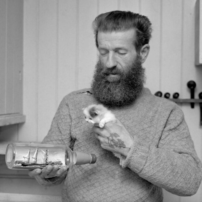 Hombre con barba sosteniendo un gato pequeño y una botella con un barco dentro, imágenes adorables de gatos históricas