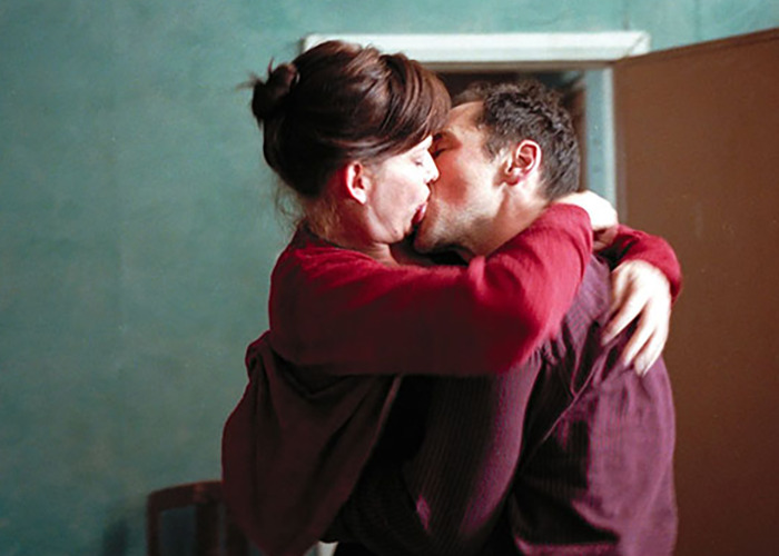 Pareja de estrellas de cine abrazándose apasionadamente y besándose durante una escena íntima en el set de filmación.