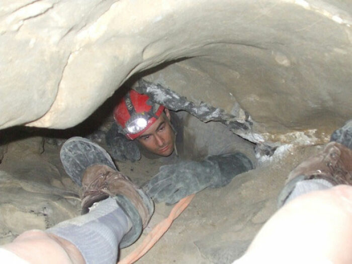 Hombre con casco y linterna explorando cueva estrecha, reflejando que Reddit no es para los débiles de corazón.
