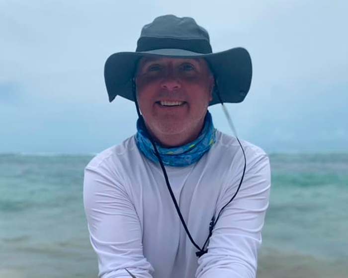 Hombre sonriente con sombrero y pañuelo cerca del agua, relacionado con safari y cornada fatal de búfalo a cazador millonario.