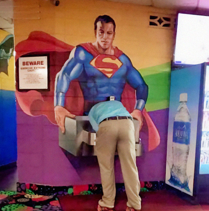 Persona usando un bebedero con diseño de Superman, ejemplo divertido de fallos de diseño en espacios públicos.
