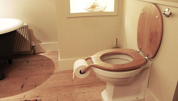Inodoro con asiento de madera y soporte para papel higiénico integrado en un fallo de diseño divertido y terrible.