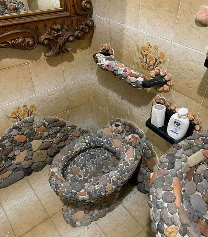 Baño con fallos de diseño divertidos y terribles, con lavabo, inodoro y barra de apoyo hechos de piedras decorativas.
