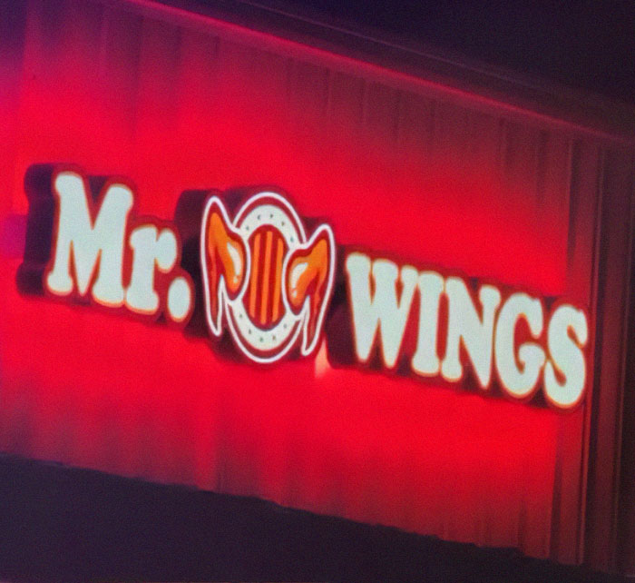Letrero con fallo de diseño en logo de Mr. Wings que genera confusión visual por la combinación de letras y gráficos.