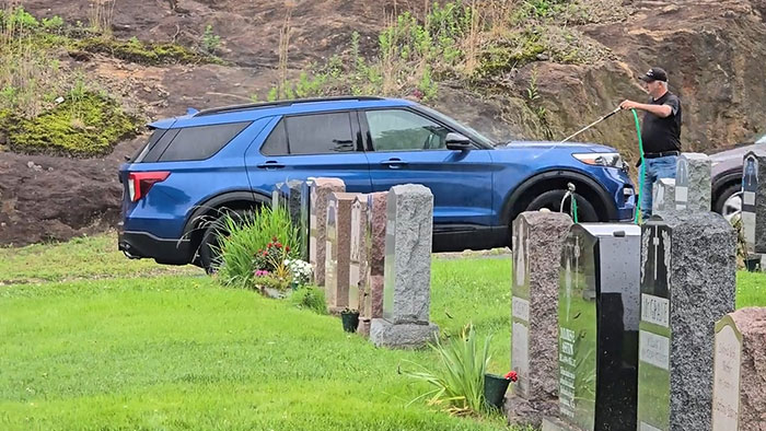 Hombre prepotente regando en un cementerio junto a un coche azul, mostrando actitud arrogante y falta de respeto.
