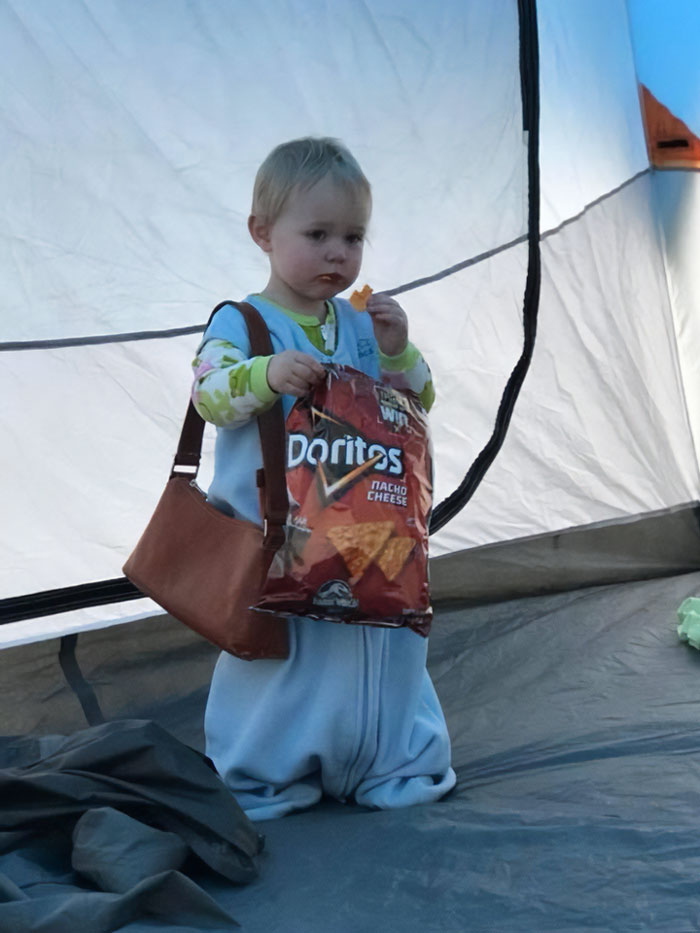 Niño pequeño en tienda de campaña comiendo Doritos con bolso marrón, imagen divertida de vacaciones de verano para compartir.
