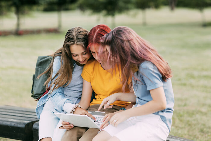 Tres chicas jóvenes usando laptop al aire libre, mostrando momentos sorprendentes en Reddit sin temor ni reserva.