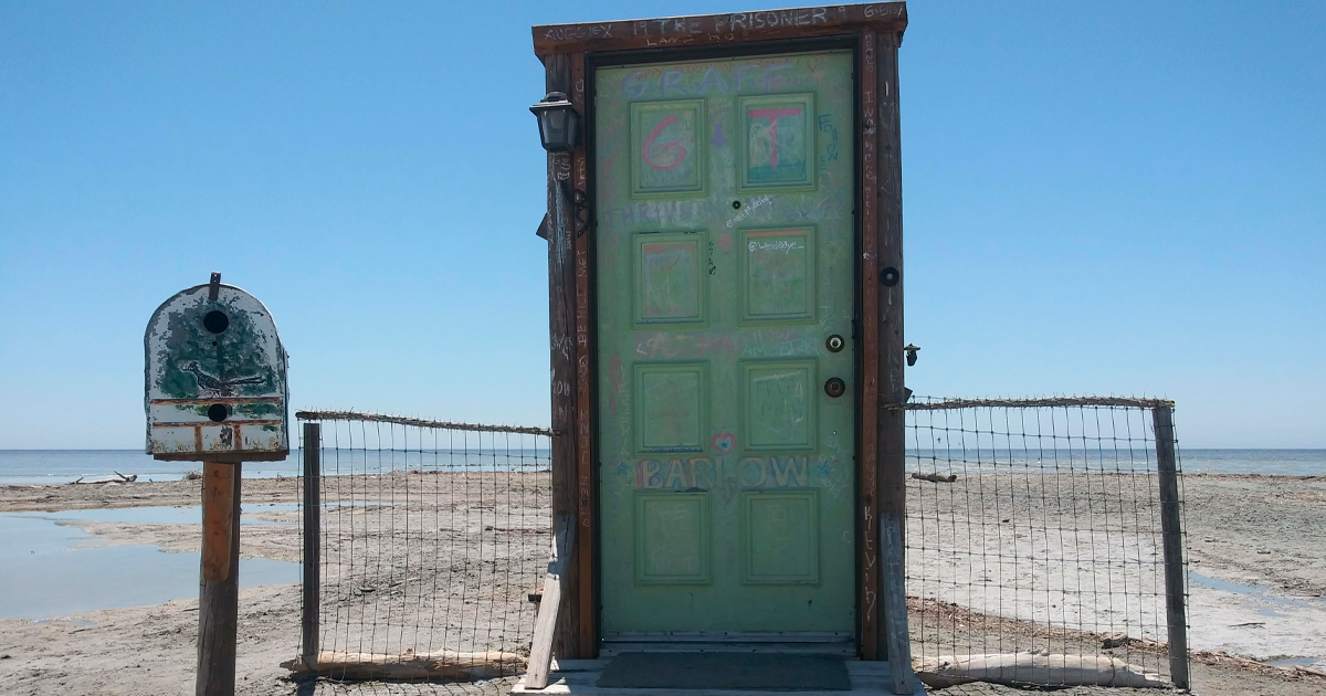 Puerta verde con graffiti y buzu00f3n viejo encontradas en la playa junto al mar y cielo despejado.