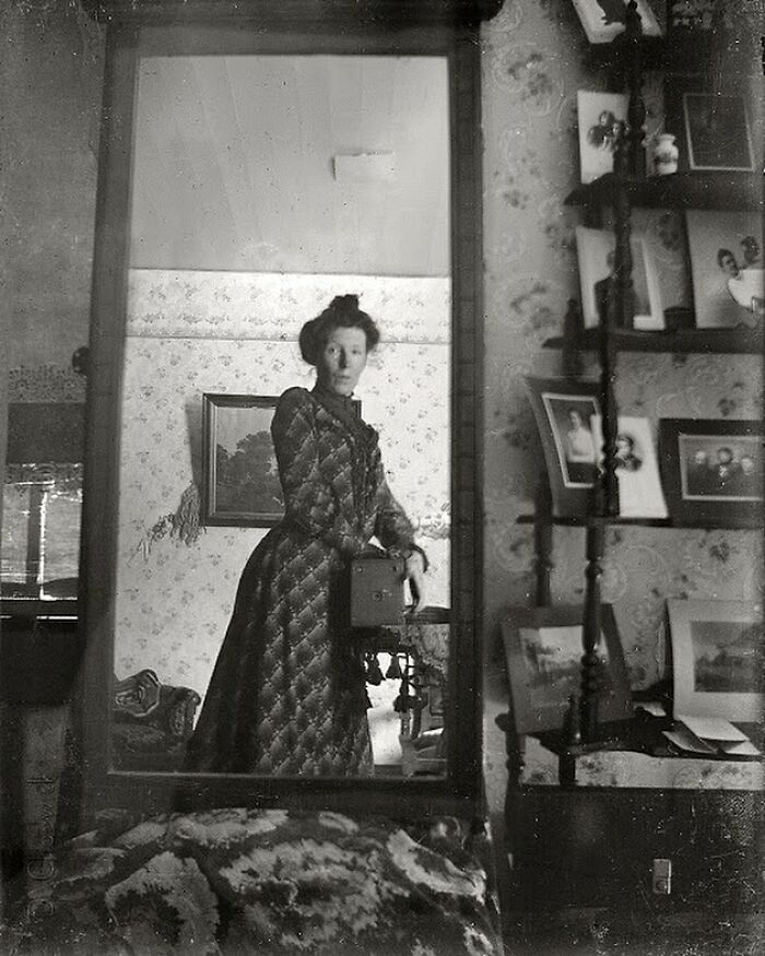 Mujer vestida con ropa antigua capturada con cámara vintage en un espejo en habitación histórica decorada con fotos y cuadros. Mujer vestida con ropa antigua capturada con cámara vintage en un espejo en habitación histórica decorada con fotos y cuadros.