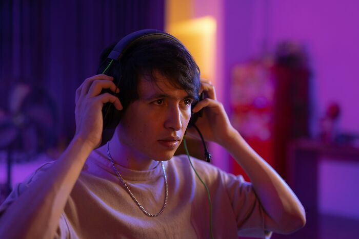 Joven concentrado con auriculares en habitación con luces de colores, mostrando intensidad típica de Reddit no apto para débiles.