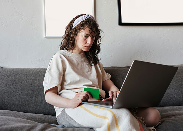 Mujer joven usando laptop en sofá, investigando sobre vacíos legales y su explotación antes de ser descubiertos.