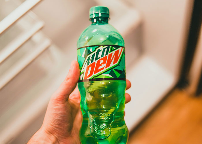 Mano sosteniendo una botella de Mountain Dew enfocada en vacíos legales explotados antes de ser descubiertos.
