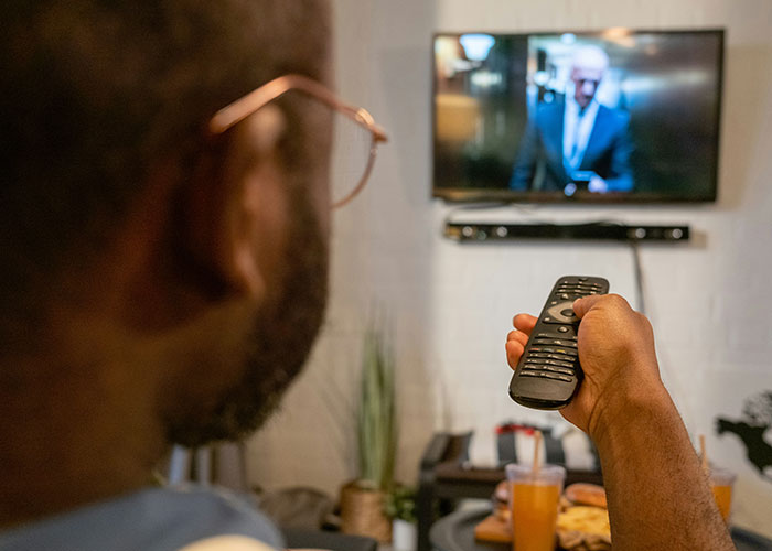 Hombre usando control remoto viendo televisión, ilustrando concepto de vacíos legales aprovechados en medios digitales.