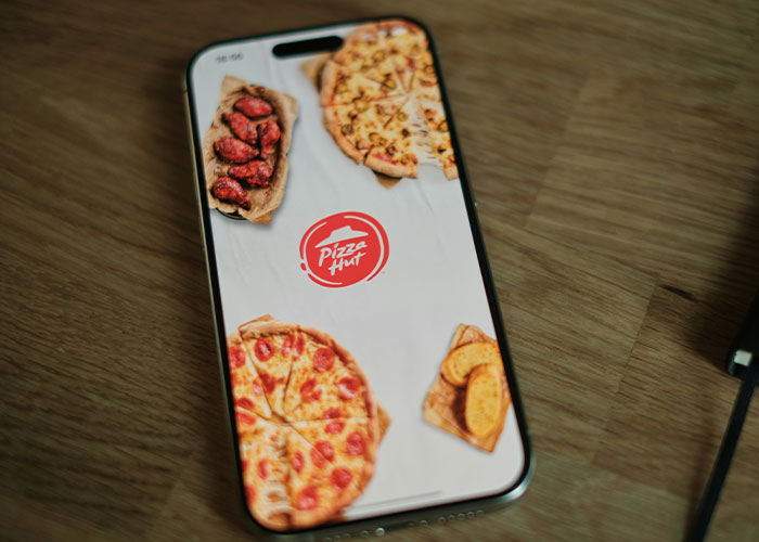 Smartphone mostrando la app de Pizza Hut con imágenes de pizzas y alitas, concepto relacionado con vacíos legales explotados.