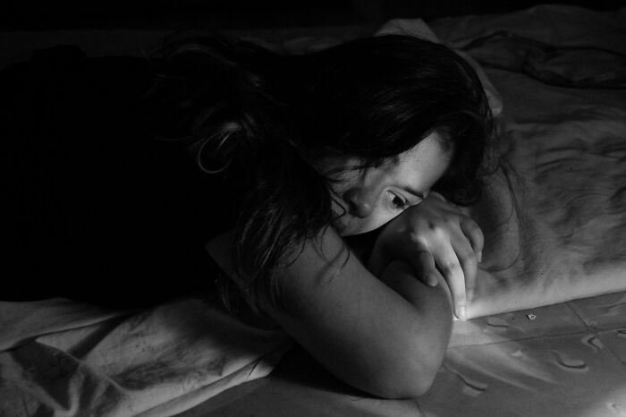 Mujer pensativa y preocupada acostada en cama en cuarto oscuro, reflejando datos inquietantes y lamentaciones personales.