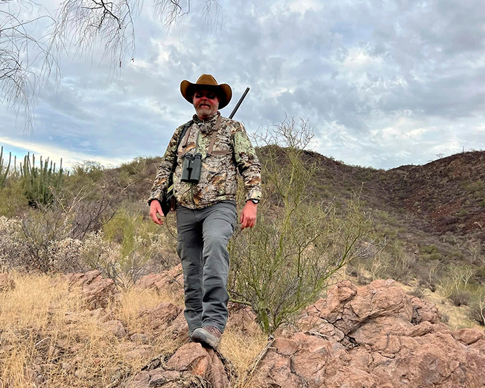 Cazador millonario en safari con ropa de camuflaje y sombrero en terreno rocoso, tragedia con búfalo fatal durante safari.