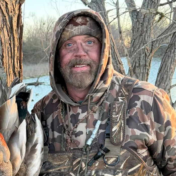 Hombre con ropa de camuflaje cerca de un lago, relacionado con safari de búfalo y cazador millonario.