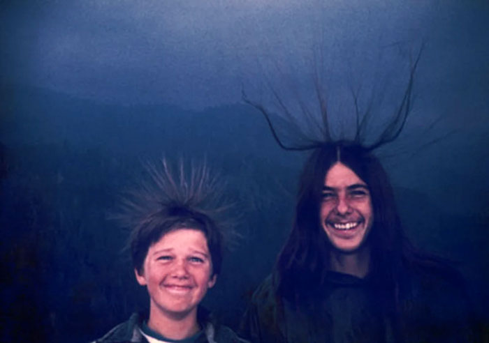 Dos chicos sonrientes con cabello erizado debido a electricidad estática en foto tomada segundos antes de un desastre inesperado.