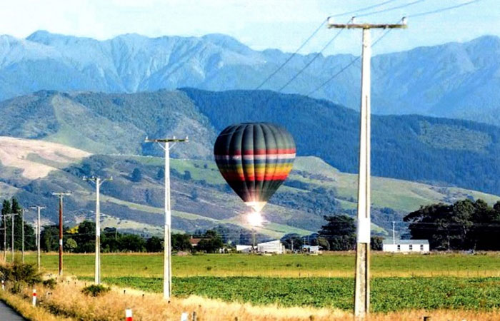 Globo aerostático a punto de chocar con cables eléctricos segundos antes del desastre en campo abierto con montañas al fondo.
