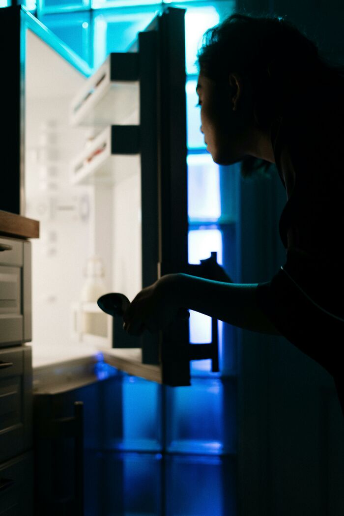 Persona mirando dentro de la nevera abierta de noche, reflejando datos inquietantes que lamentan haber aprendido.