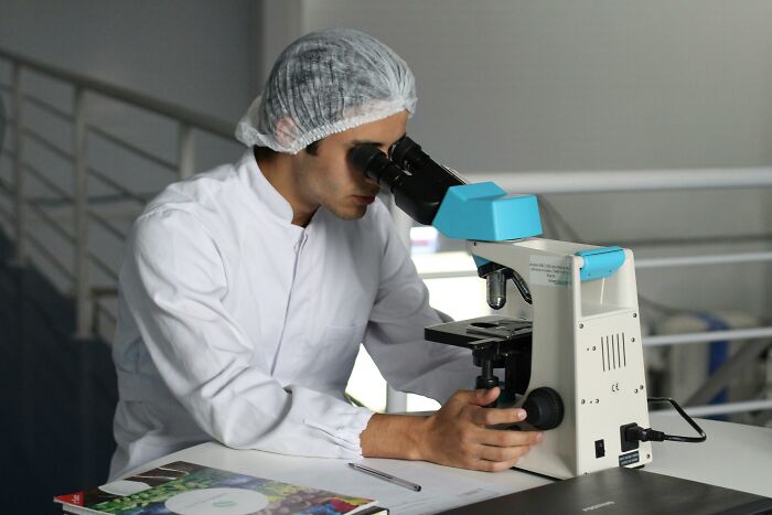 Científico usando microscopio en laboratorio analizando datos inquietantes que lamentan haber aprendido.