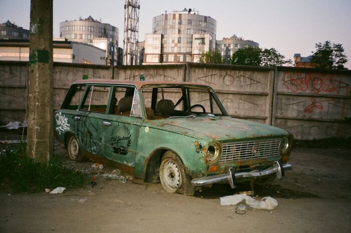 Coche antiguo oxidado abandonado en un terreno vacío con grafitis en la pared, simbolizando secretos ocultos y olvidados.