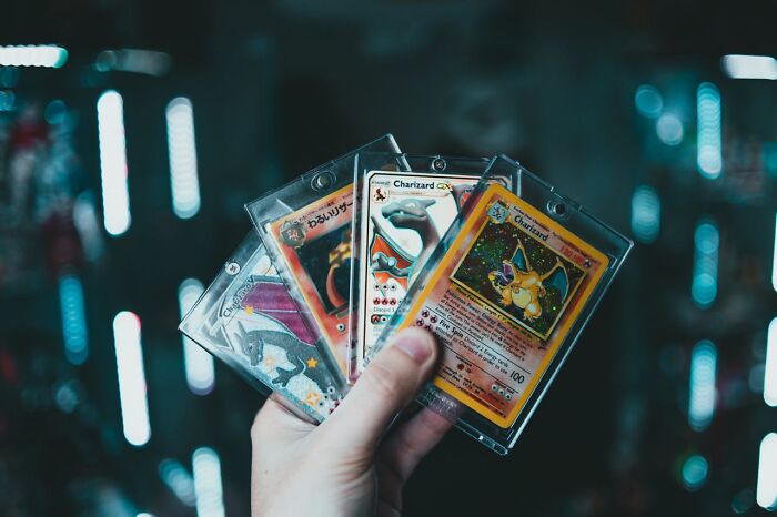 Mano sosteniendo cartas de Charizard en fundas transparentes, compartiendo pequeños secretos coleccionables.