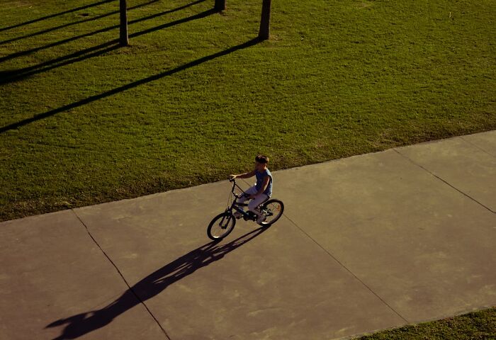 Niño montando bicicleta solo en un camino del parque bajo la luz del sol, ilustrando secretos pequeños compartidos.