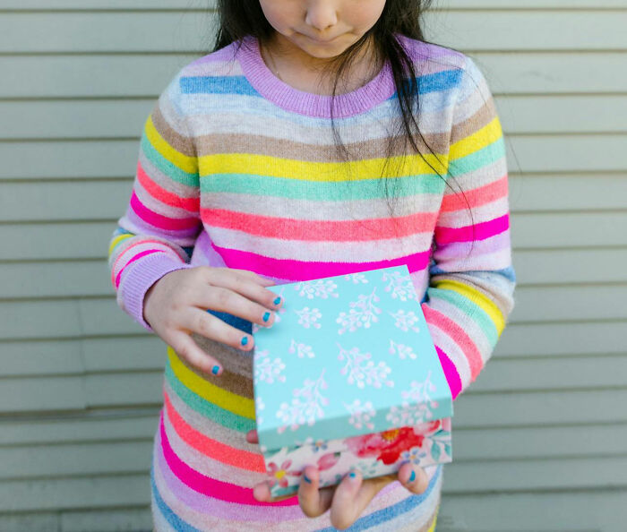 Niña adolescente con suéter de rayas coloridas sosteniendo una caja floral, imagen relacionada con padres cotillas y adolescentes.