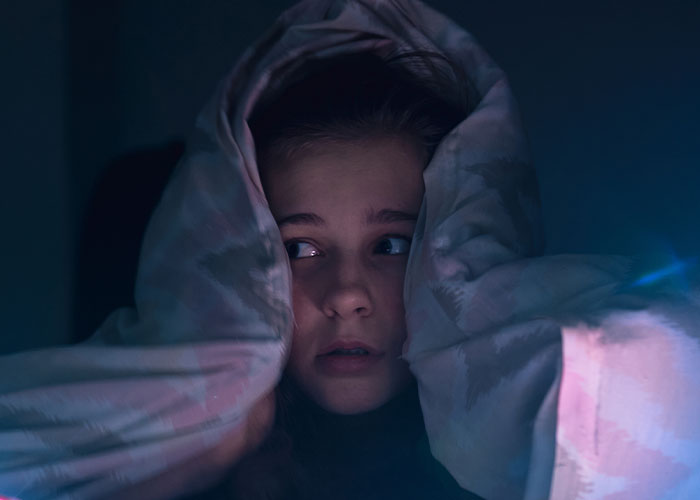 Niña asustada cubriéndose con una manta en la oscuridad, representando encuentros con maldad pura sobrevividos.