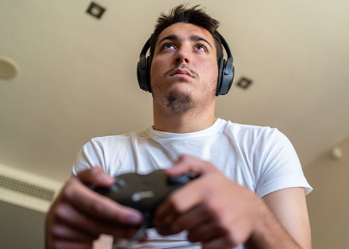 Joven con auriculares y camiseta blanca jugando videojuegos, experimentando momentos de encuentro con el mal puro.