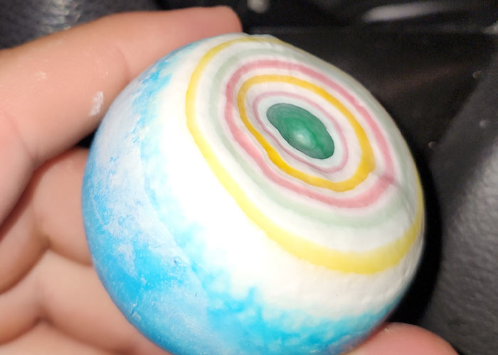 Mano sosteniendo una pelota con capas de colores concéntricos, simbolizando encuentros con maldad pura y supervivencia.