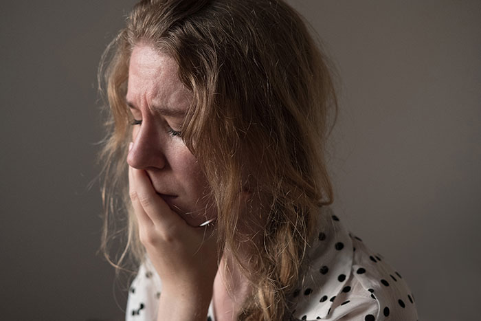 Mujer triste con expresión de angustia reflexionando sobre experiencias con un psicópata en su infancia en un entorno tenue.