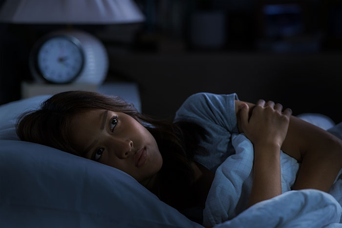 Mujer despierta en la cama con expresión pensativa, ilustrando experiencias con un psicópata durante la infancia.