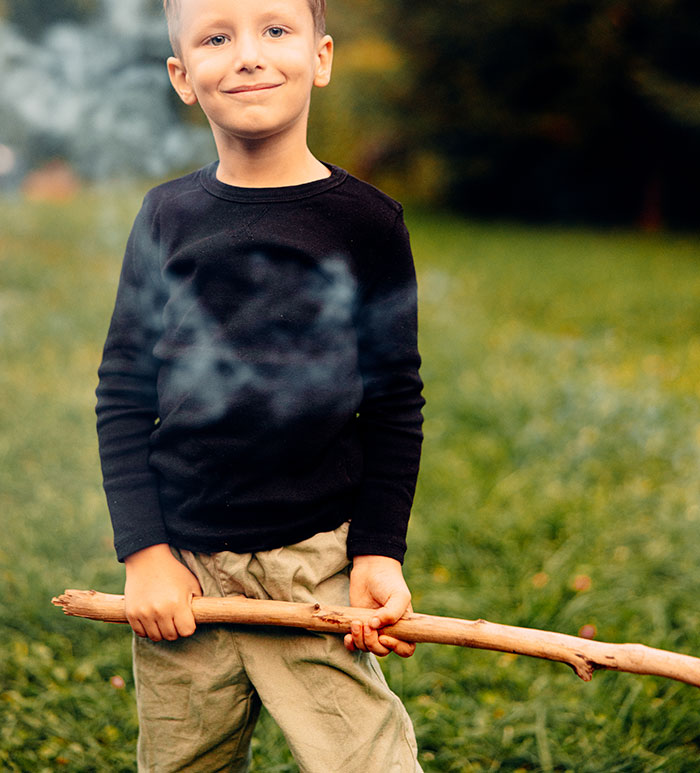 Niño sonriente con suéter negro y pantalones beige sosteniendo un palo en un campo, relacionado con psicópatas y experiencias aterradoras.