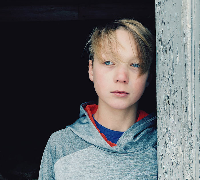 Niño con expresión seria apoyado en una pared, reflejando emociones de quienes crecieron con un psicópata cerca.