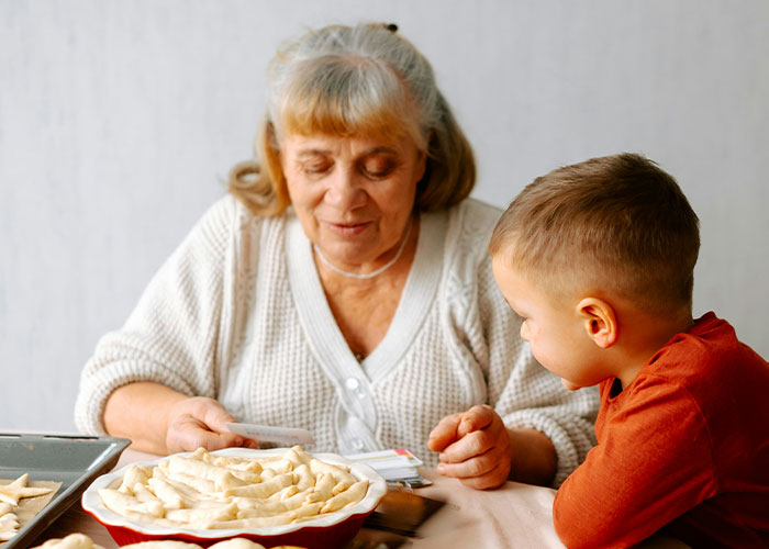 Mujer mayor y niño preparando masa juntos, imagen relacionada con experiencias que soportan con sus suegras.
