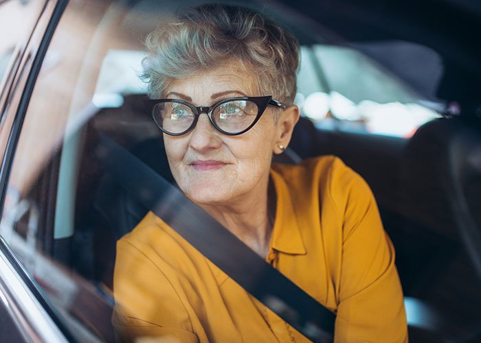 Mujer mayor con gafas y camisa amarilla sentada en un coche con cinturón de seguridad, reflejando relaciones con suegras.