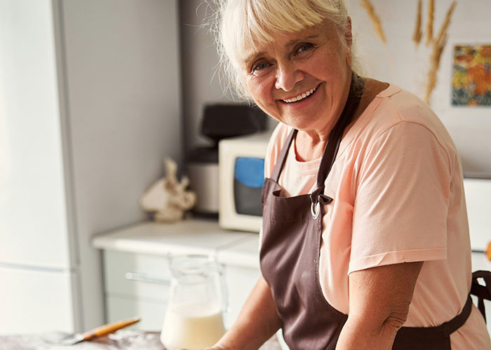 Mujer mayor sonriente en cocina, representando situaciones que soportan las personas con sus suegras.